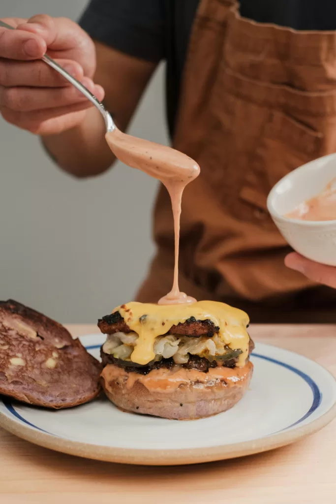 man pouring sauce on burger